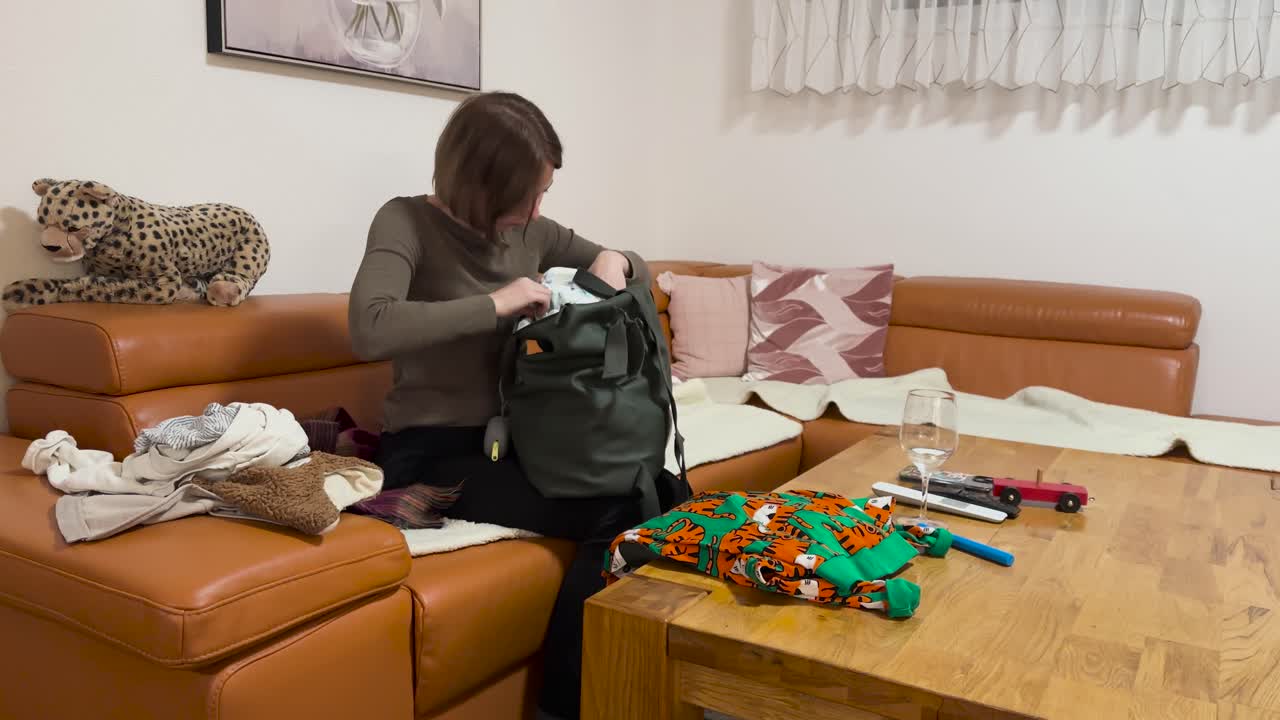 A mother sits at home and searches through a bag to find diapers, surrounded by baby items. Concept of parenting, childcare routine, organization, and everyday family life