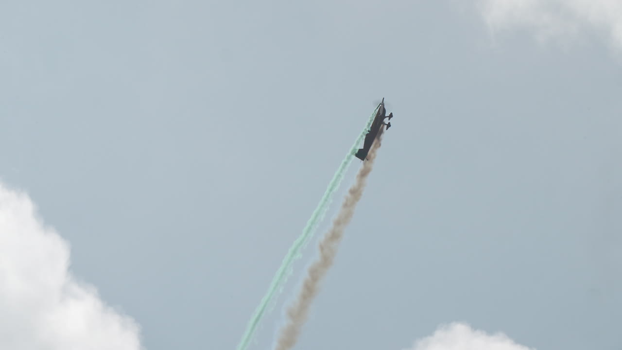 Aerobatic airplane performing a vertical climb with colored smoke trail before imitating engine off stall at the top