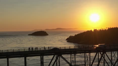 Shot-of-pedestrians-enjoying-the-sunset-on-Deception-Pass-bridge-while-cars-drive-by-in-the-foreground