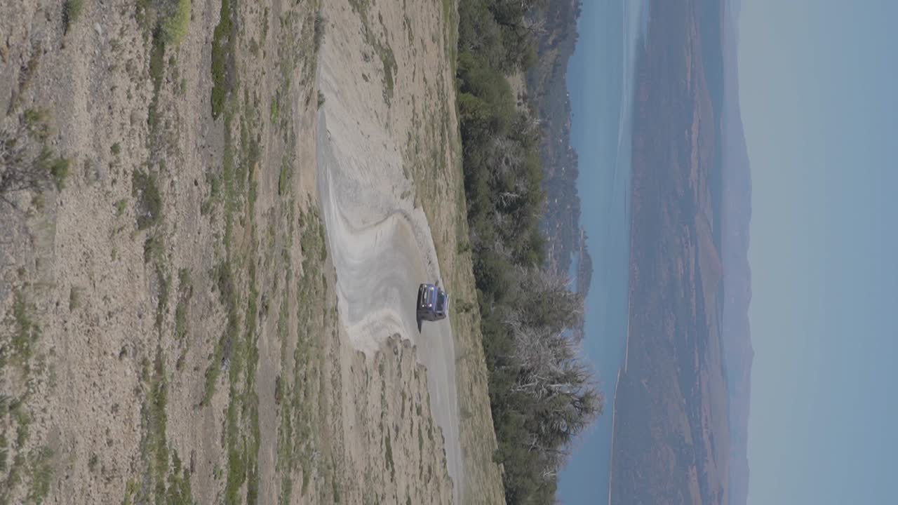 un auto circulando por una carretera en las colinas de patagonia, argentina con montañas y un lago al fondo