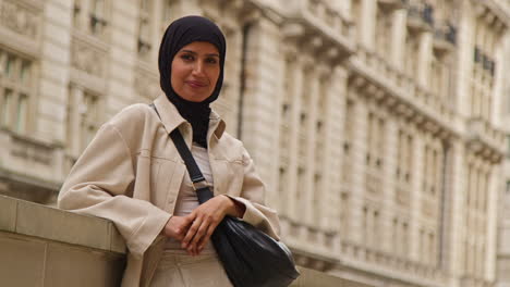 portrait of smiling muslim businesswoman wearing hijab and modern business suit standing outside city office buildings 10