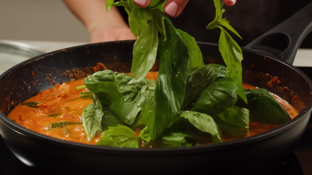 Adding Fresh Basil Leaves to Simmering Red Sauce in a Pan