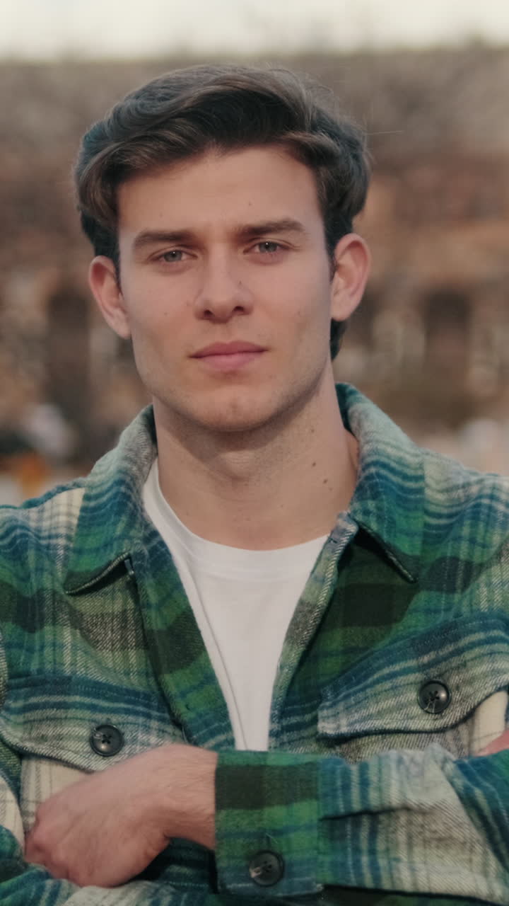 Young man crosses his arms looking at camera on old city background