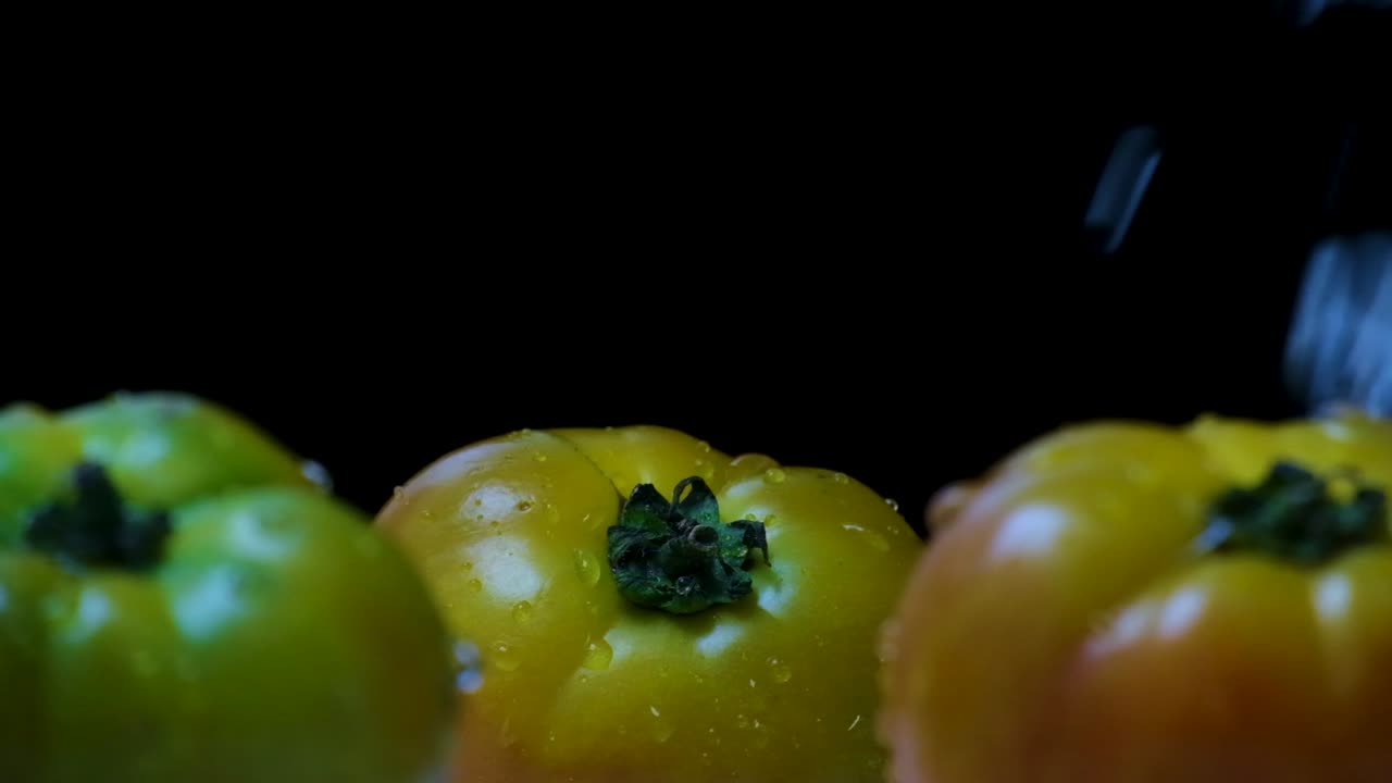 disparo en cámara lenta de tomates grandes amarillos y verdes siendo salpicados de lluvia, frente a un fondo negro