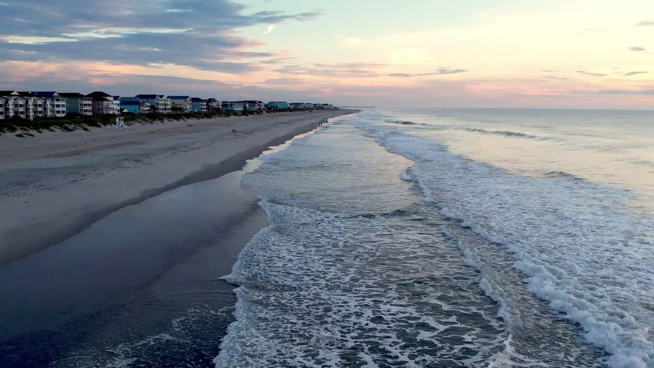 Ripresa aerea bassa del surf e delle onde che si infrangono a Carolina Beach, Carolina del Nord all'alba