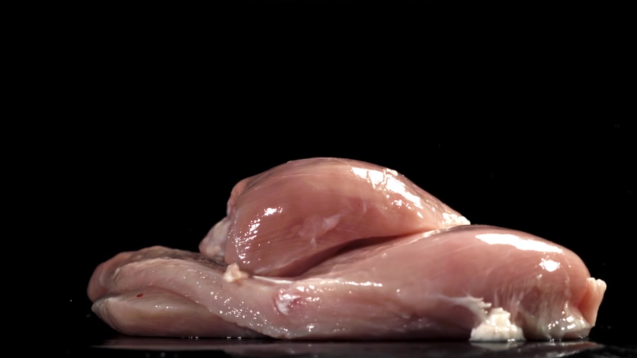 Petti di pollo crudi che cadono al rallentatore su una superficie nera