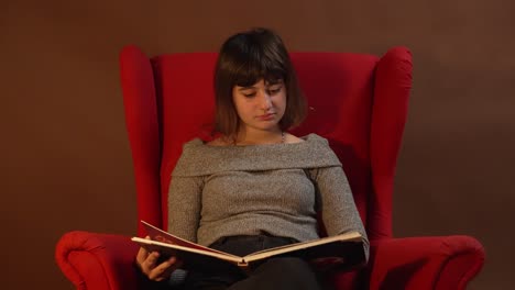 una niña sentada en una silla roja mientras lee un libro de cuentos navideños