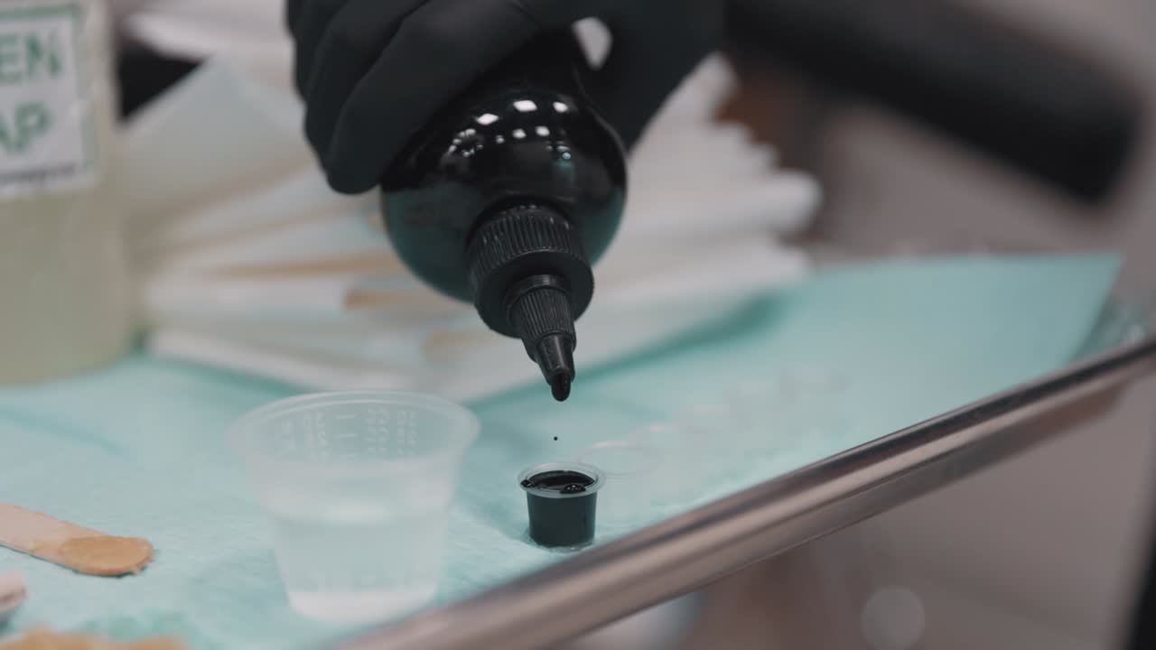 Black ink drips in slow motion into a container, in a tattoo shop