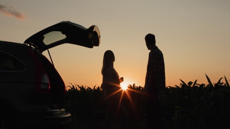 Una-Pareja-Joven-Admira-La-Puesta-De-Sol-Sobre-El-Campo,-Parada-Cerca-De-Su-Auto