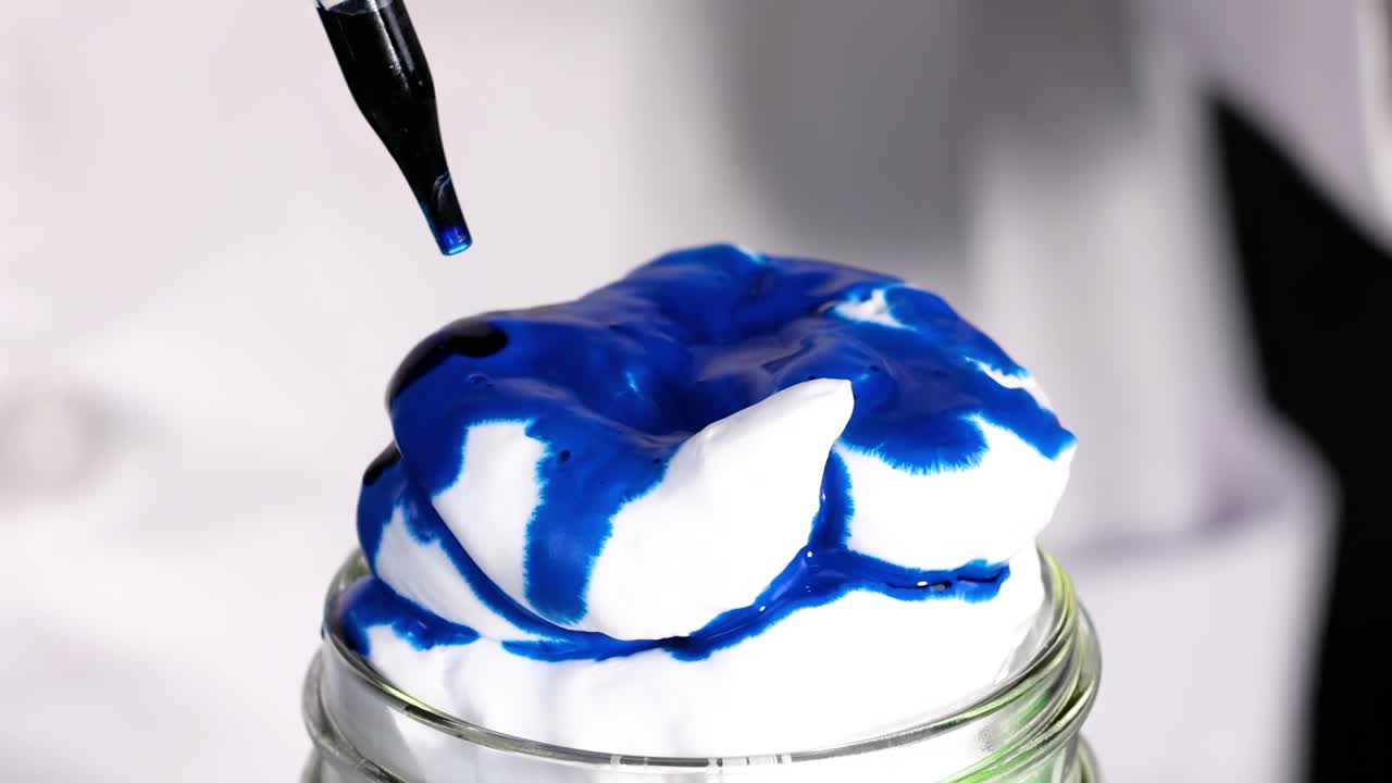 Watch blue dye create mesmerizing patterns on fluffy shaving cream in a glass jar.