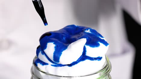 watch blue dye create mesmerizing patterns on fluffy shaving cream in a glass jar.
