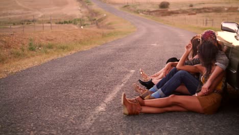 boho style friends rest leaning against vintage convertible on road