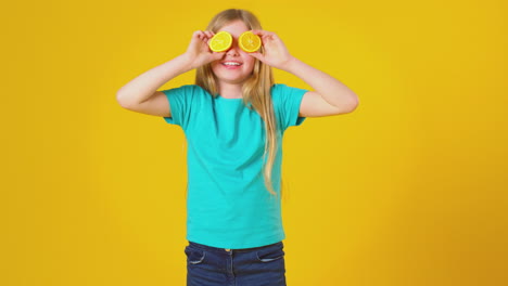 retrato de estudio de una niña con dos mitades naranjas frente a los ojos contra un fondo amarillo