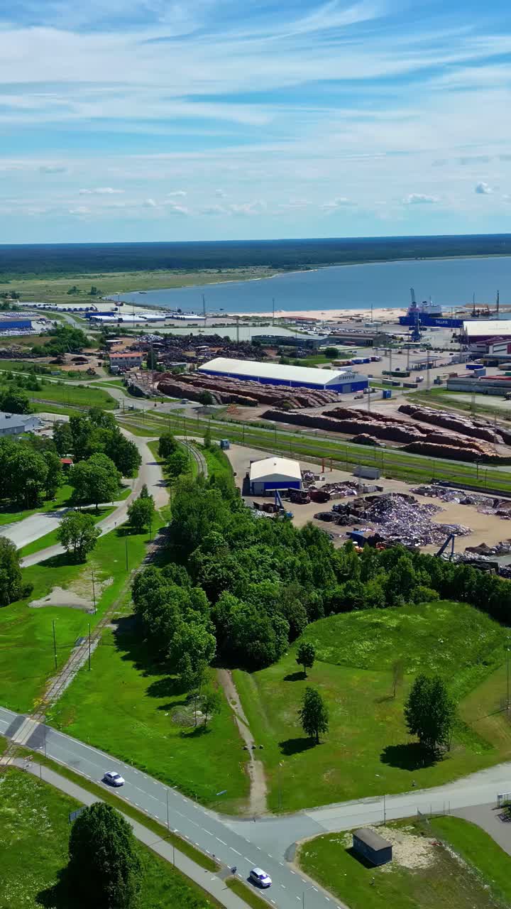 Coastal industrial area with stacked timber and port buildings near calm sea, aerial