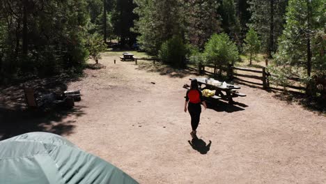 low aerial shot flying over tent and following camper to picnic table where she folds a towel