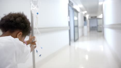 african american girl with drip walking in hospital corridor, slow motion, copy space