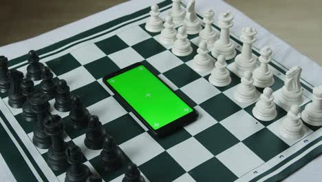 piezas de ajedrez blancas y negras y un teléfono inteligente de pantalla verde en el medio. concepto de aplicación de ajedres