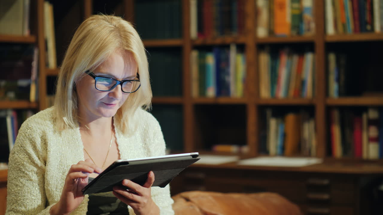 A Woman Reads A Book In A Tablet Sits In The Luxurious Back Of The Library