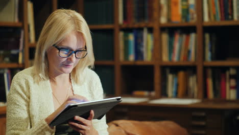 a woman reads a book in a tablet sits in the luxurious back of the library