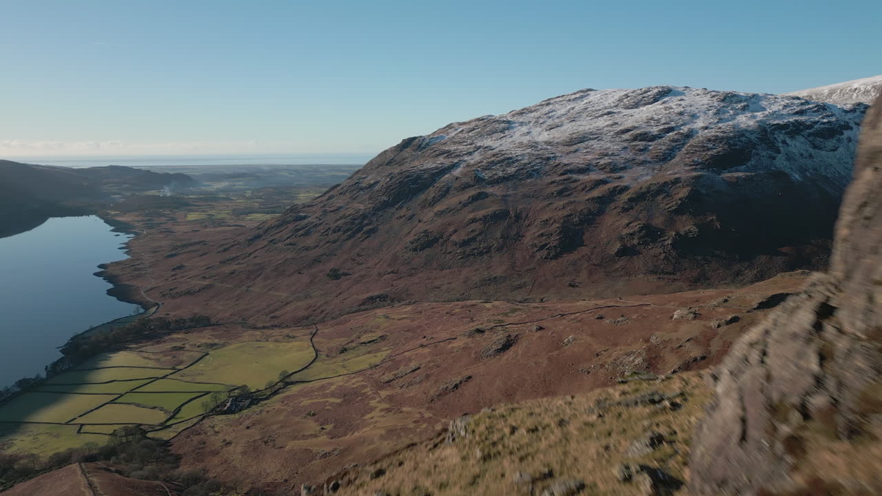 Escursionista seduto sul fianco di una montagna, mentre un sorvolo rivela una valle verde, montagne e un lago a Wasdale, Lake District, Regno Unito
