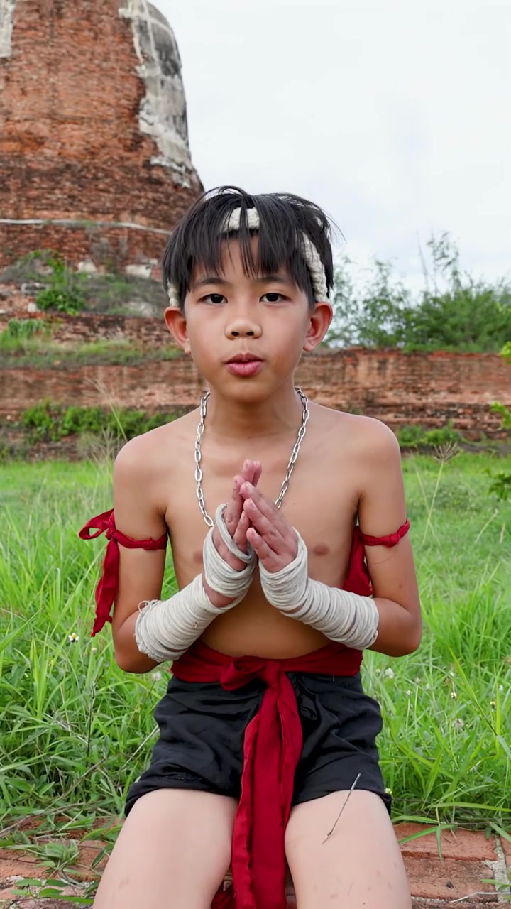 Anak laki-laki Asia dengan pakaian seni bela diri tradisional berlutut dan membungkuk di depan reruntuhan pagoda bata kuno