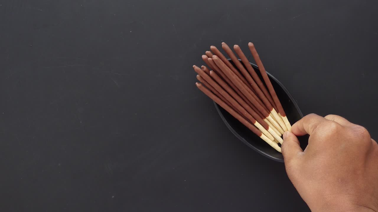la mano recogiendo palos de galletas cubiertos de chocolate sobre un fondo negro