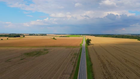 drone flight over golden wheat fields and country road on a sunny summer day with rainbow in the sky peaceful latvian countryside aerial view