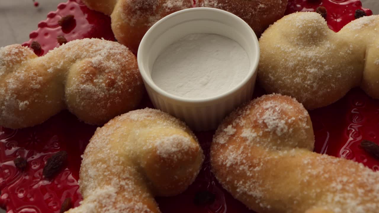 cámara moviéndose sobre una configuración para fotografía de alimentos, bollos de navidad suecos recién horneados con azúcar y pasas en un plato rojo ornamentado