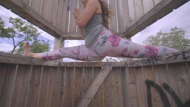 Donna caucasica in spaccata yoga all'aperto, ripresa inclinata dal basso.