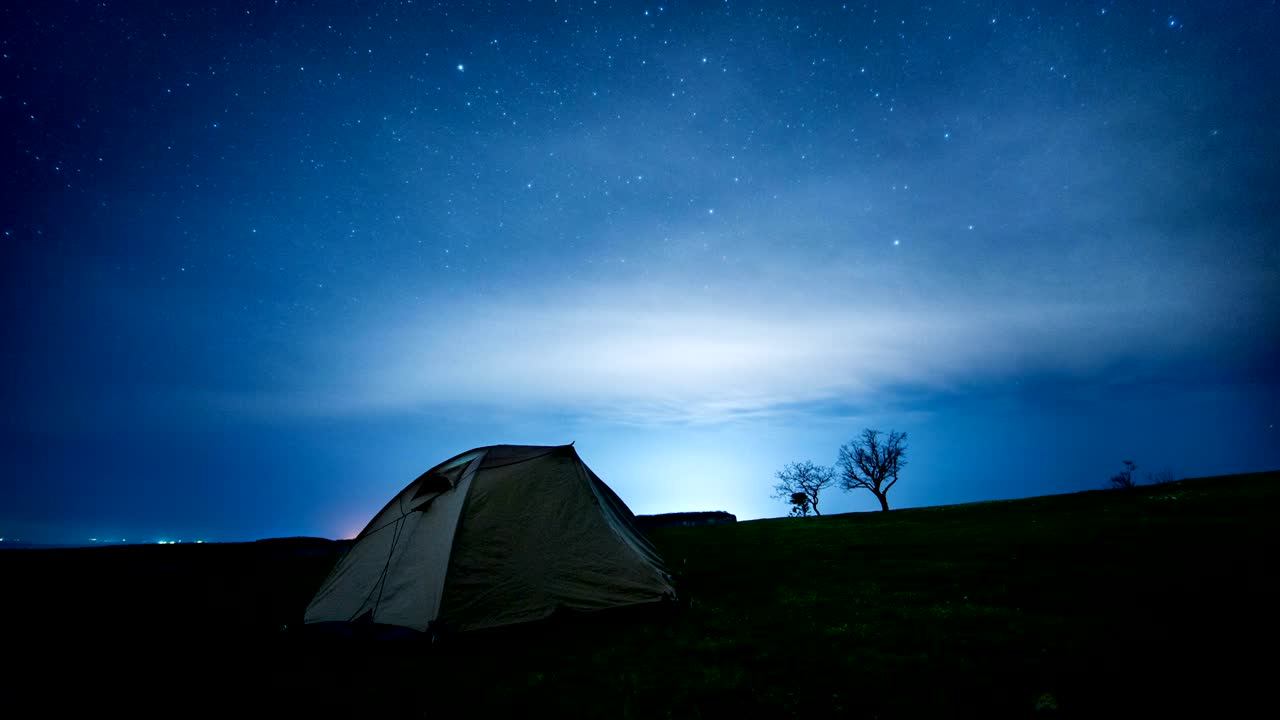 time-lapse. una tienda de campamento brillante en las montañas nocturnas bajo los senderos de las estrellas.