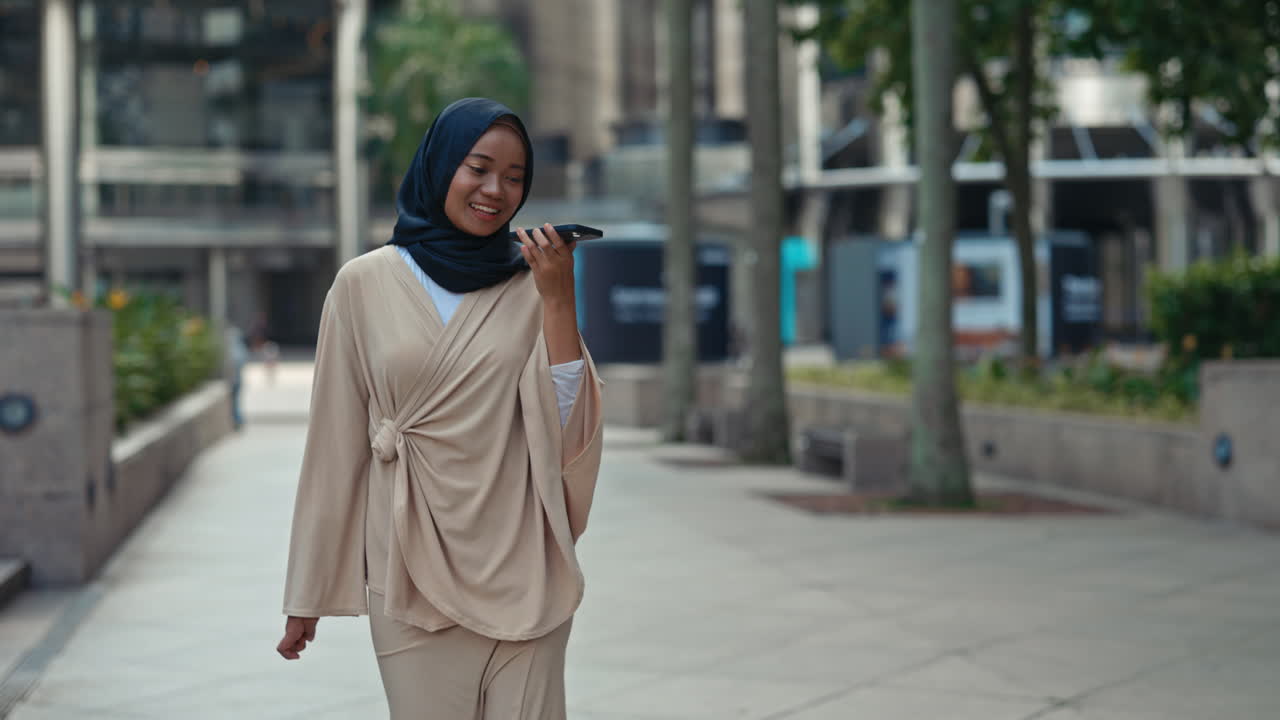 Young woman in hijab walking and talking on a smartphone in a city