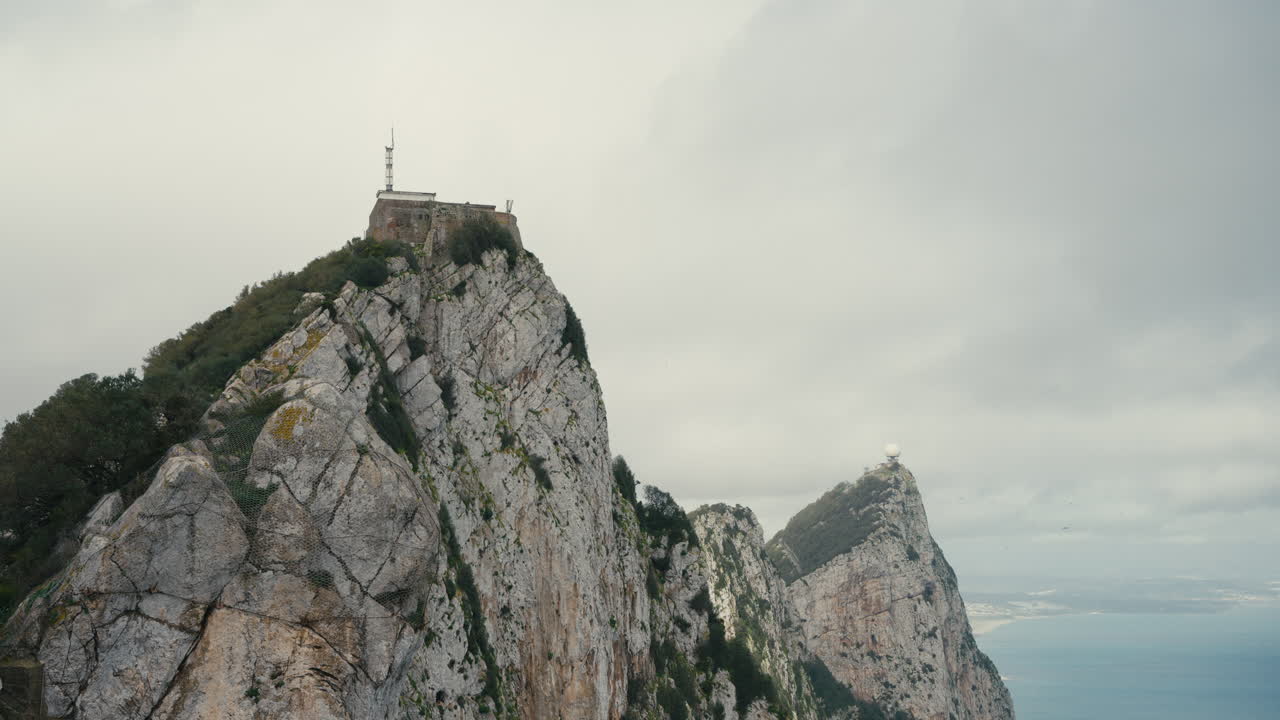 Ripide scogliere calcaree della Rocca di Gibilterra, con la Batteria di O’Hara e la cupola radar sopra il Mediterraneo sotto cieli nuvolosi.