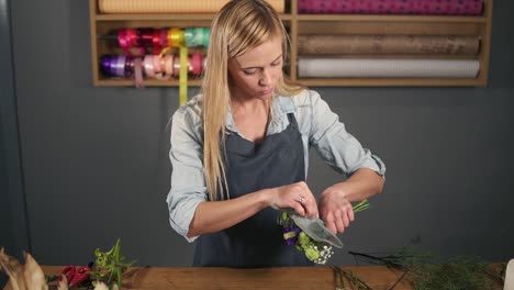 Young-beautiful-female-florist-wrapping-a-bunch-of-flowers-in-decorating-paper.-Slow-Motion-shot