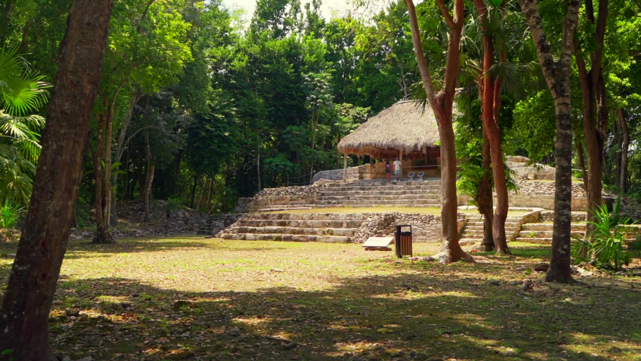 Una panoramica rivela antiche rovine Maya e una fitta vegetazione della giungla con turisti irriconoscibili che visitano la Struttura IV nel sito archeologico di Oxtankah.