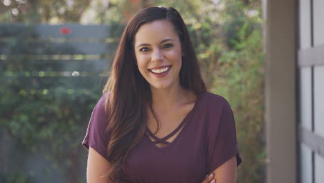 portrait of smiling young hispanic woman in garden at home against flaring sun