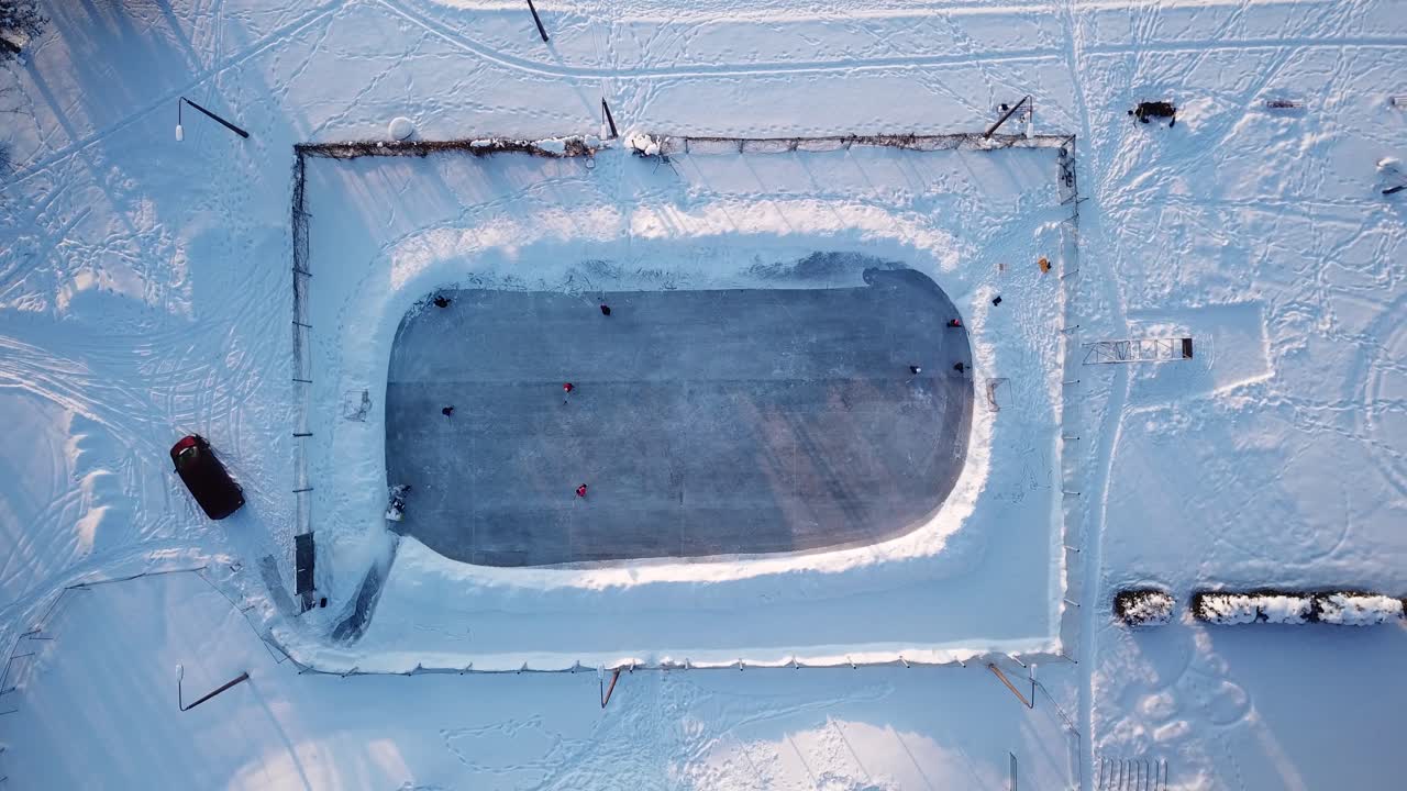 gente patinando sobre hielo y jugando al hockey en una pista de hielo al aire libre durante una puesta de sol, tiro estático de un dron