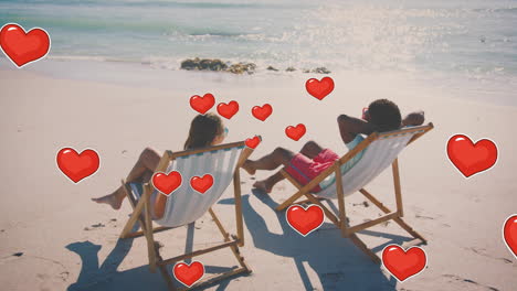 animation of hearts moving over diverse couple in love in deckchairs on beach in summer