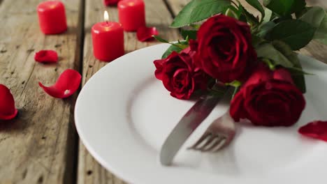 candles and red roses on plate on wooden background at valentine's day