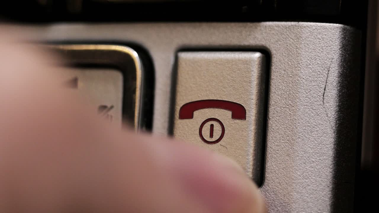 Close up finger presses red end call key on grey phone keypad