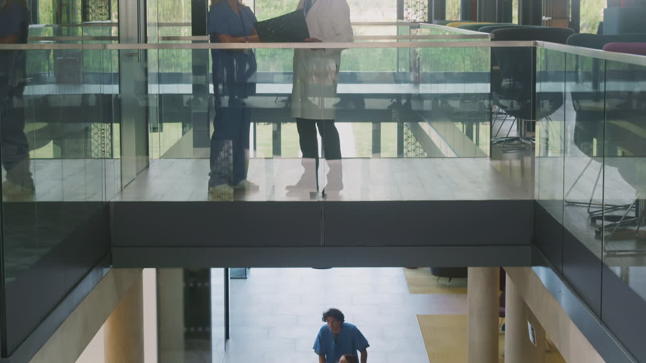 Camera Tracks Down From Doctors Discussing Scan To Patient Being Pushed In Wheelchair In Hospital