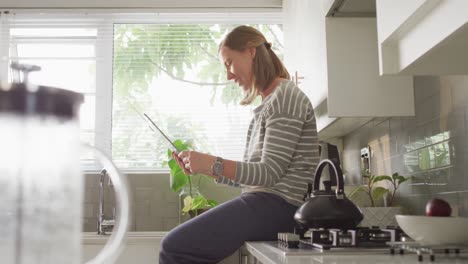 caucasian woman blowing a kiss while having a videocall on digital tablet in the kitchen at home