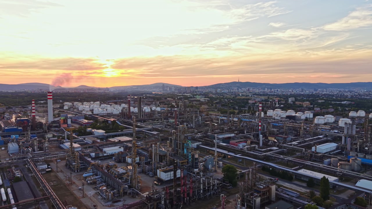 Solnedgang over et industriområde med fabrikker og raffinerier i bakgrunnen nær en by