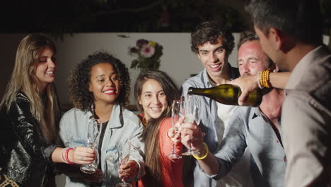 Man-popping-champagne-and-pouring-it-into-friends-glasses