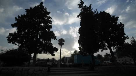 Time-lapse-of-clouds-and-blue-sky-over-silhouettes-of-trees-traffic-and-pedestrians--