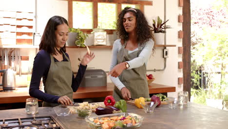two multiracial female friends preparing vegetables in kitchen, smiling and cooking, at home