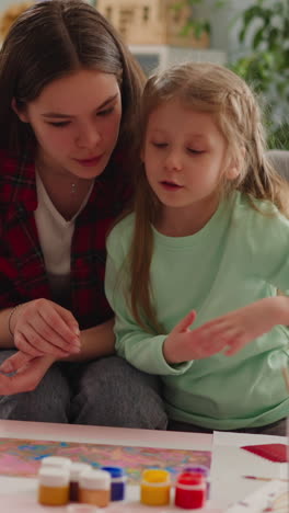 curious little girl talks about picture in erbu style with careful elder sister sitting on sofa slow motion. turkish design technique for family