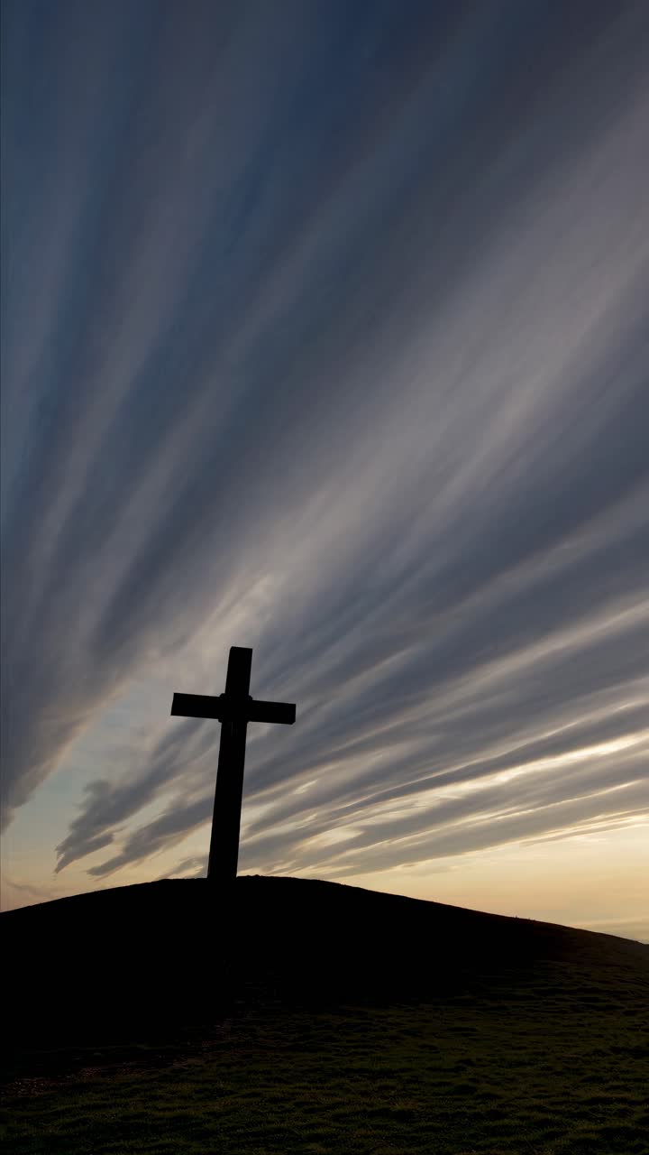 Silhouette of a cross on a hill at sunset, captured from a low angle