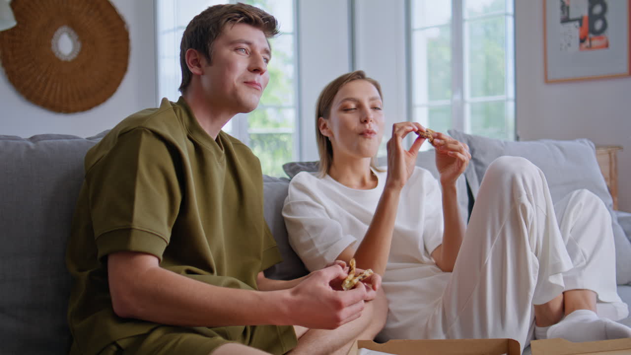 Eating boyfriend girlfriend talking at couch zoom on. Happy friends watching tv