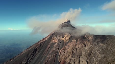 aerial: volcano in guatemala erupts dark smoke and ash on blue sky day