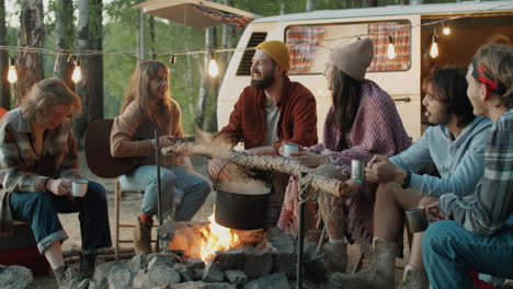 jóvenes amigos felices charlando alrededor del fuego del campamento